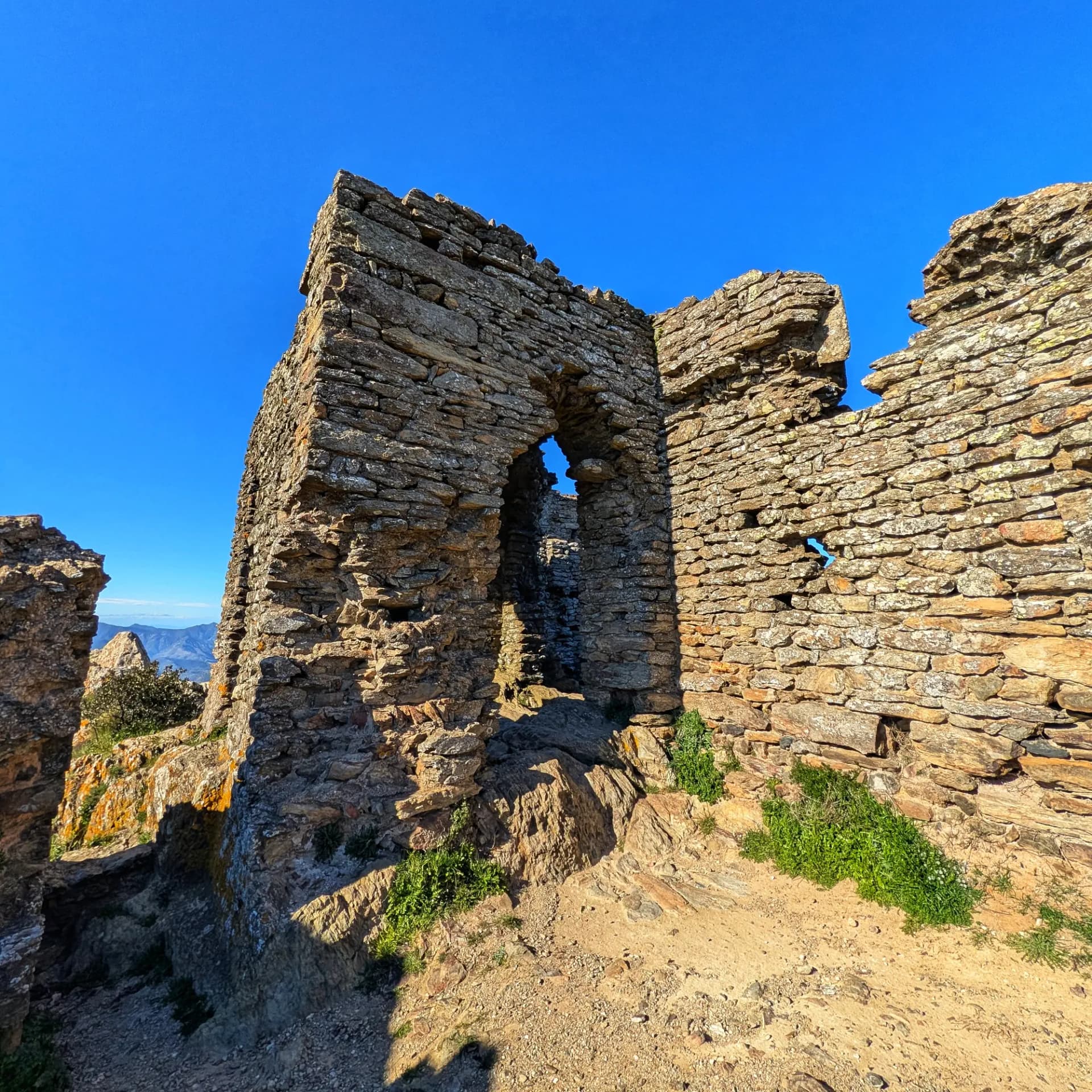 Ruïnes de pedra del Castell de Verdera amb una arcada sota un cel blau intens.