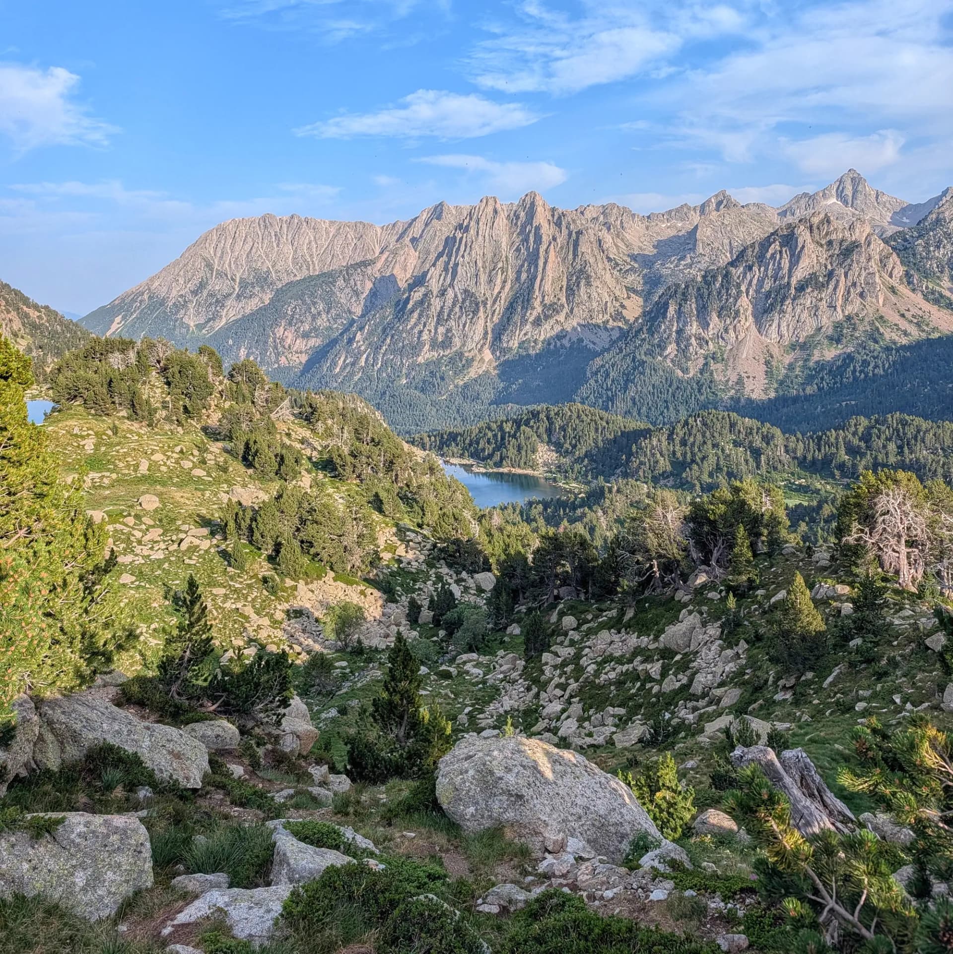 Vista panoràmica d'un llac de muntanya blau profund envoltat de boscos de pins i pendents rocosos, amb cims escarpats.