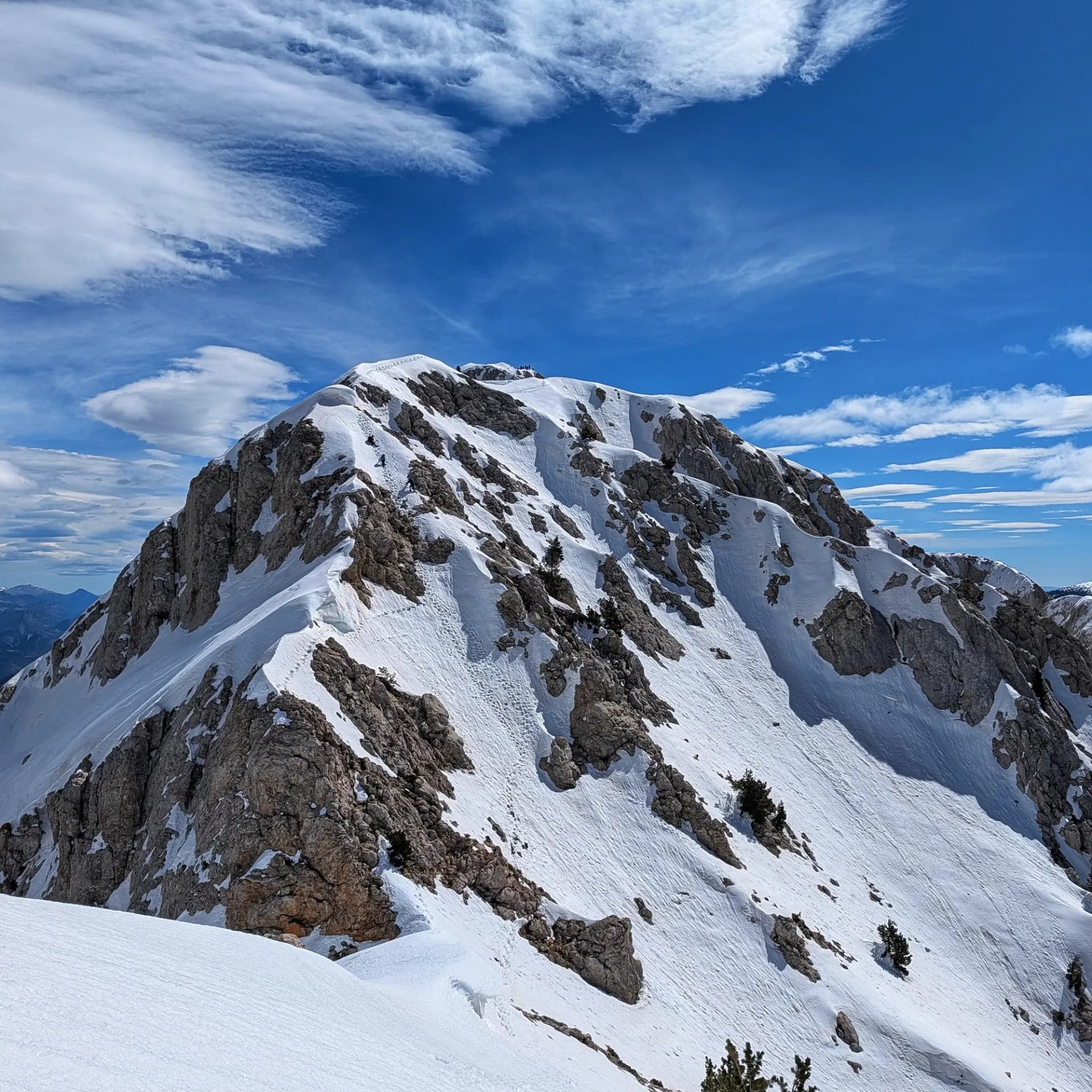 Cim nevat del Pollegó Superior al Massís del Pedraforca, amb roques, petjades a la neu i cel blau amb núvols.