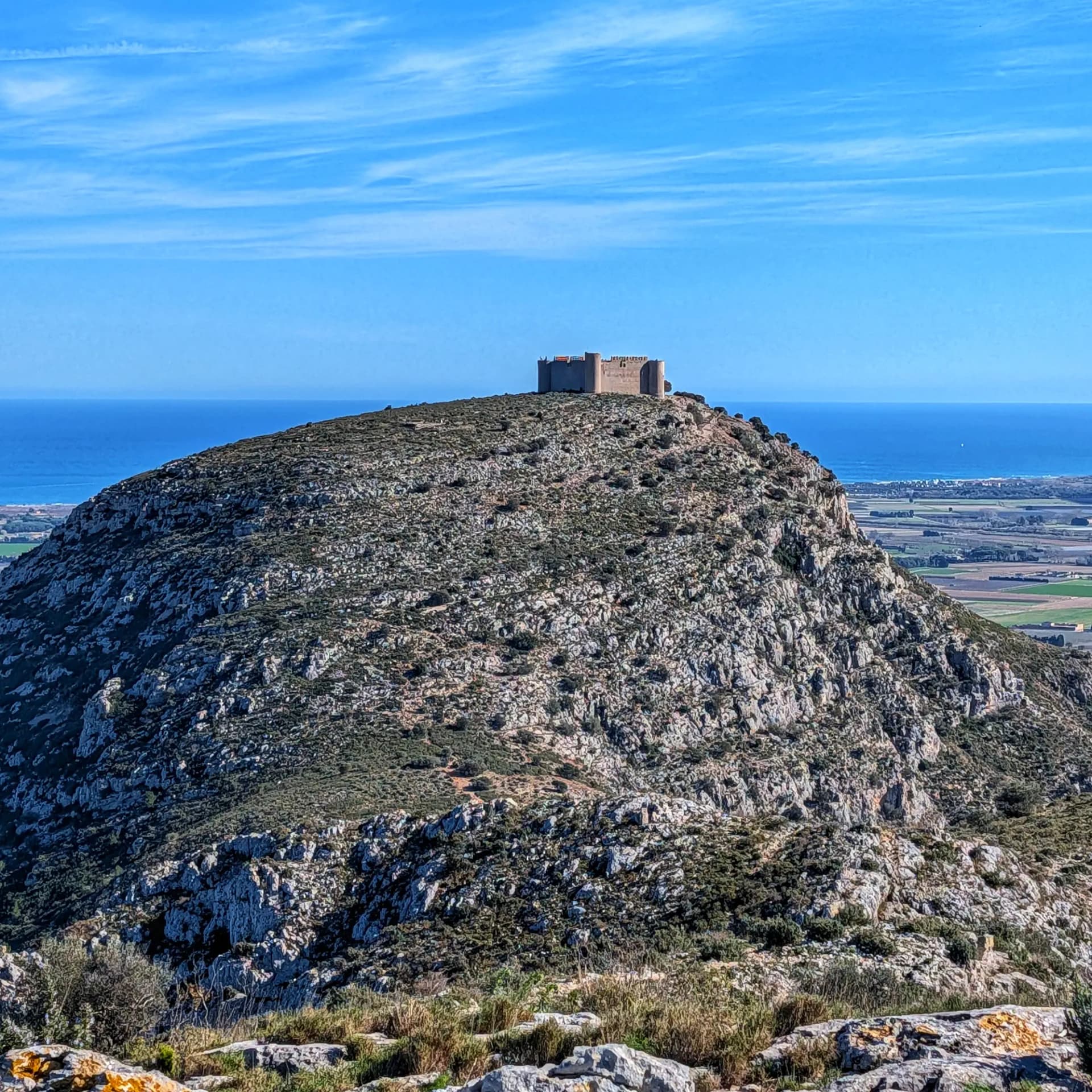 Fortaleza del Castillo de Montgrí en un cerro rocoso, con mar Mediterráneo y llanuras costeras bajo cielo azul.