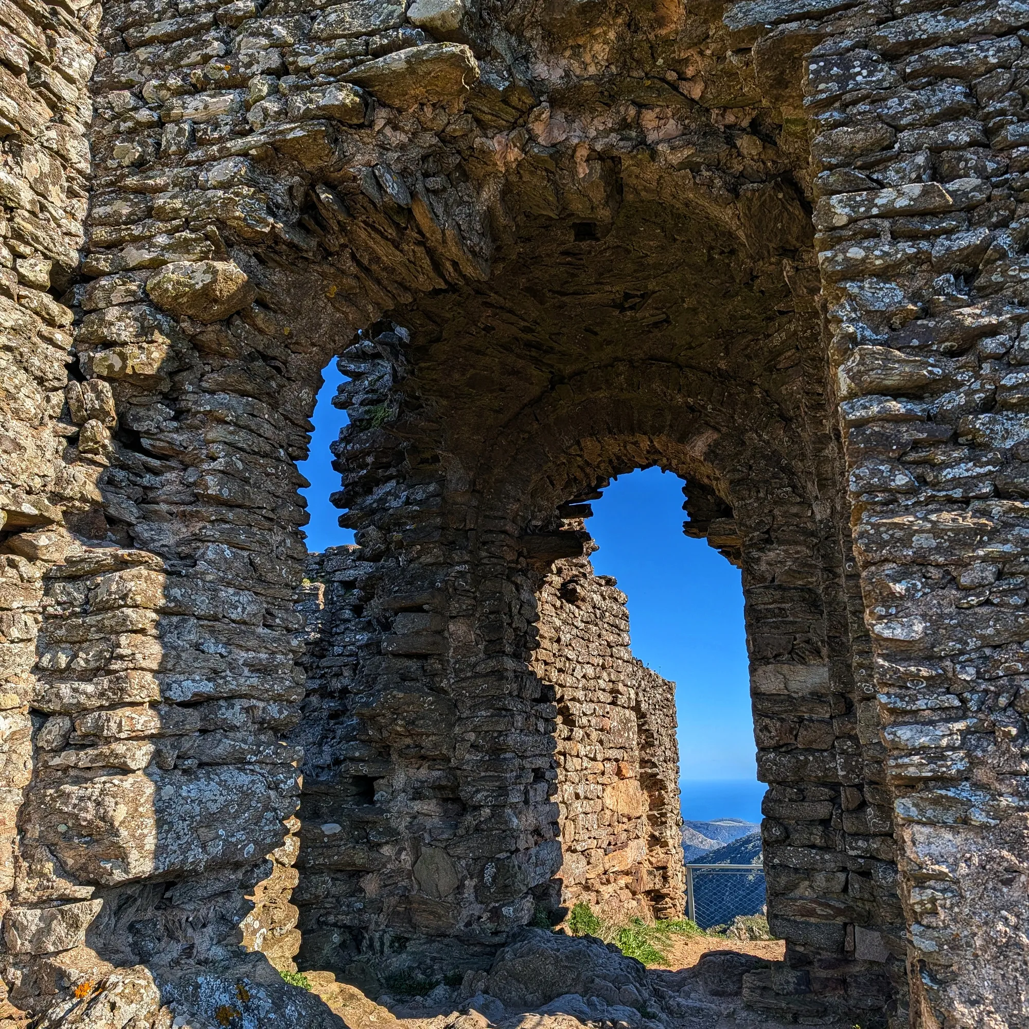 Arcs de pedra d'un castell en ruïnes amb cel blau i vista llunyana del mar Mediterrani a Verdera.