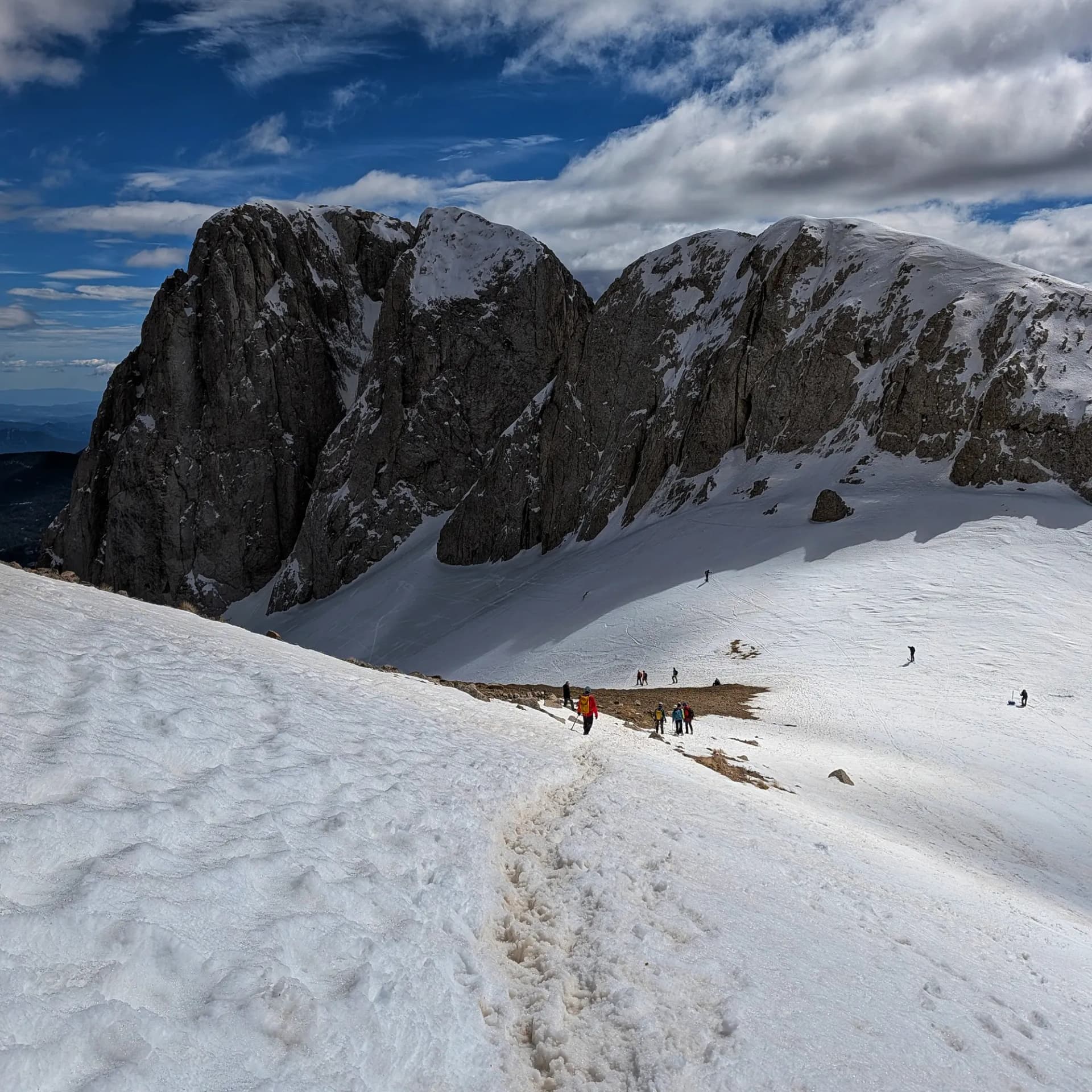 Senderistes a l'Enforcadura del Pedraforca amb el Pollegó Inferior cobert de neu i un cel parcialment ennuvolat.