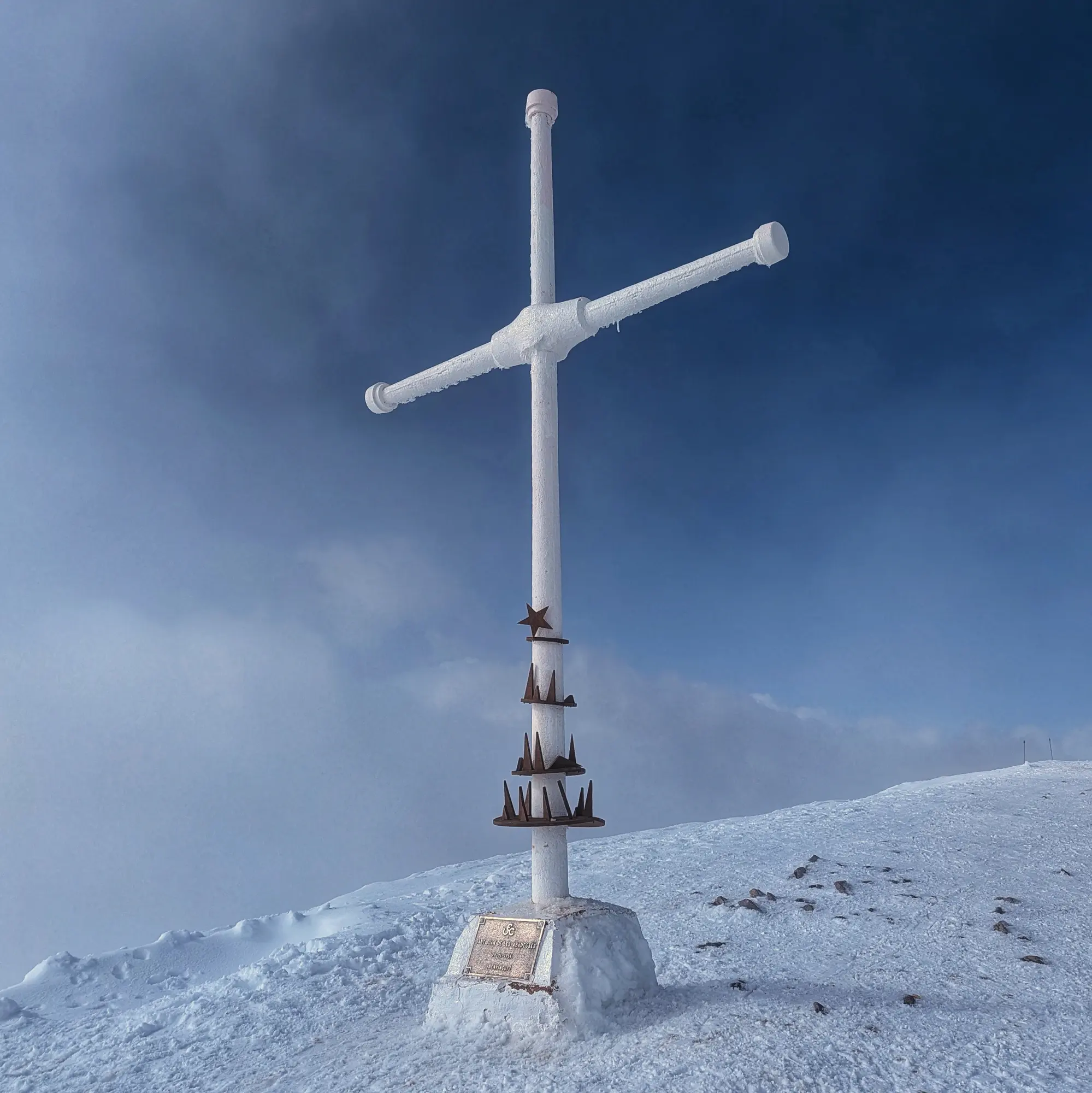 White cross on snow-covered Taga summit with partially cloudy sky.