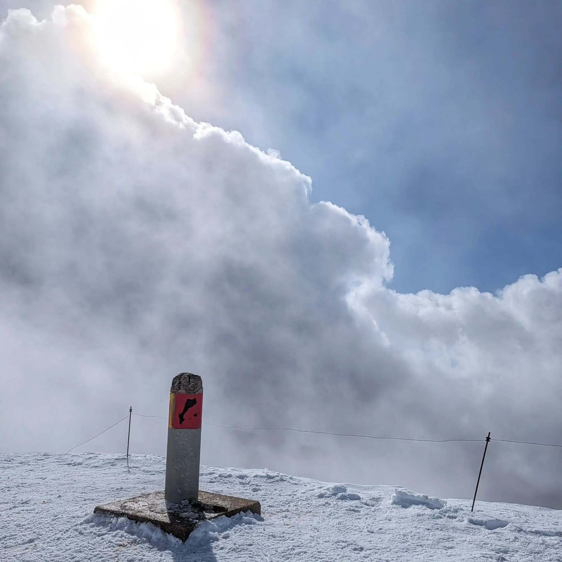 Geodetic vertex on snowy Taga summit with cloudy sky.