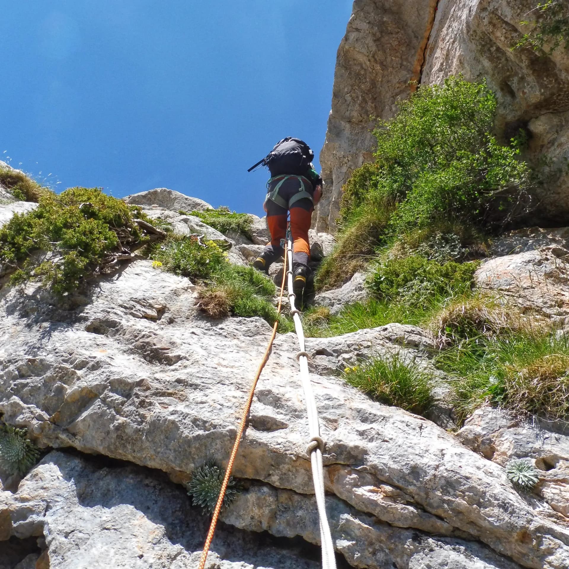 Hiker using fixed ropes to ascend a rocky section of Pedraforca's Gran Diagonal route.