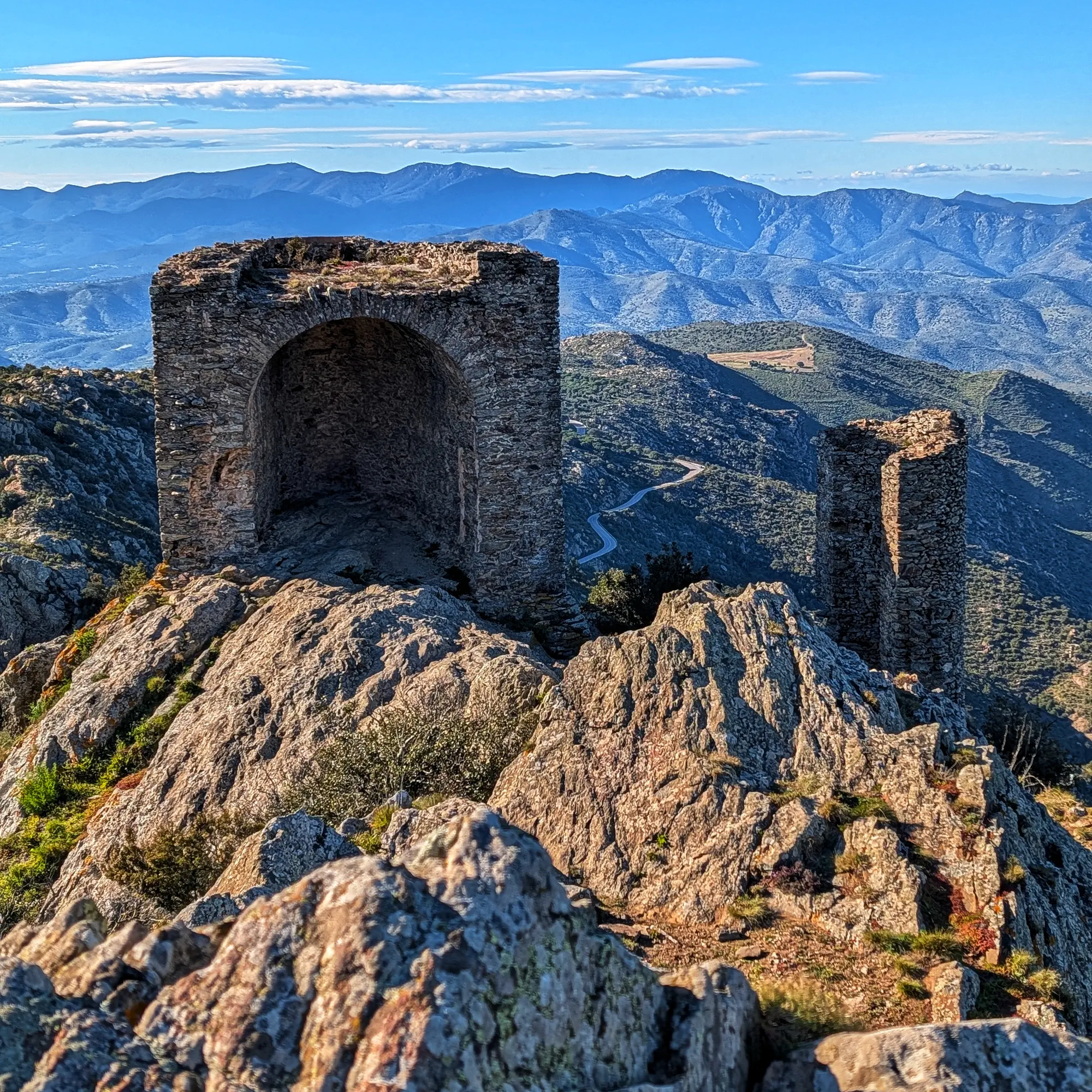 Ruïnes de pedra del Castell de Verdera en un cim rocós, amb muntanyes esglaonades i cel blau al fons.