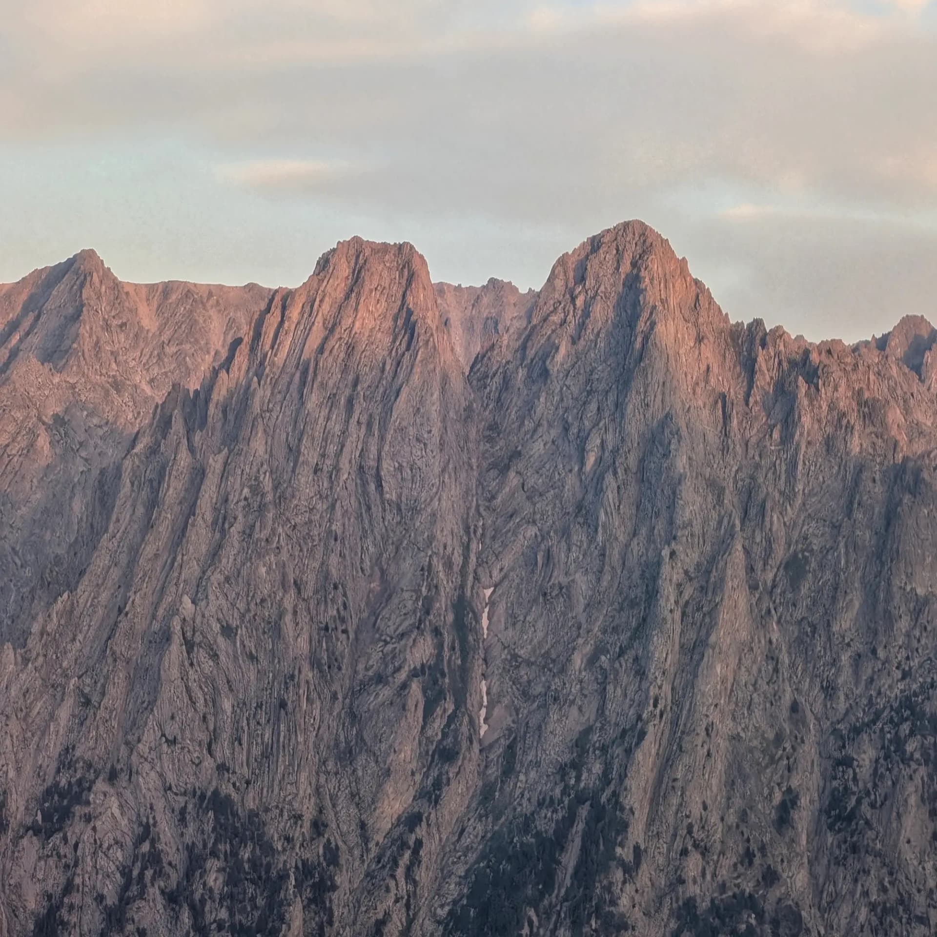 Pics de muntanya escarpats il·luminats per una càlida llum daurada al capvespre sota un cel blau-gris suau. Roques texturades.