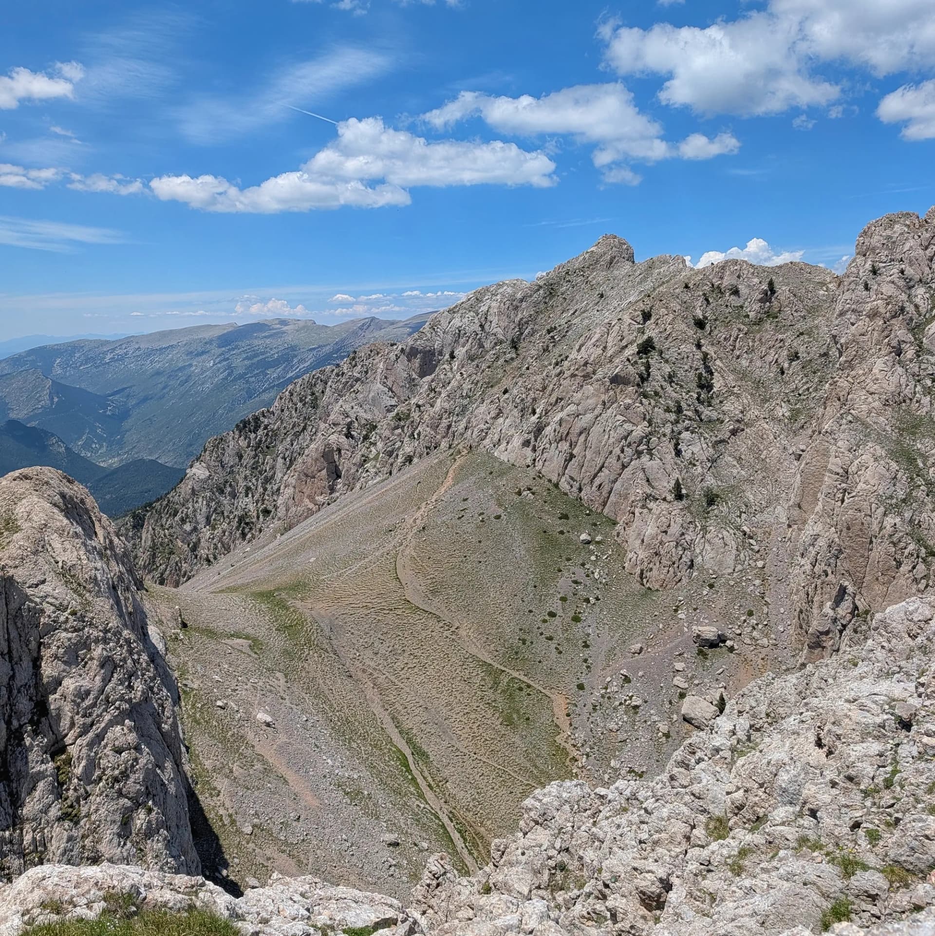 Pedraforca's rocky saddle seen from Pollegó Inferior, with blue sky and white clouds.