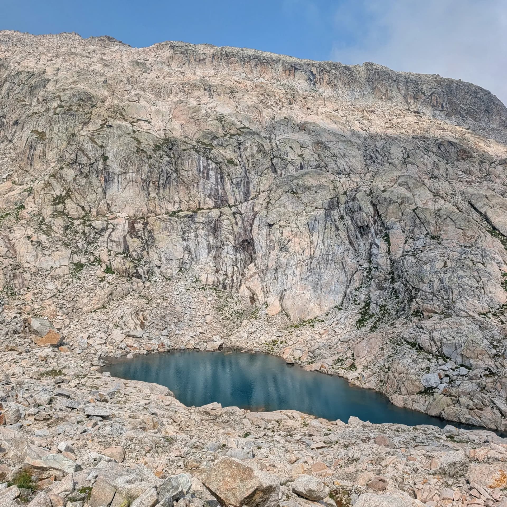 Estany d'alta muntanya en un paisatge de granit massiu i tarteres, part de la ruta d'ascensió al Pic de Comaloforno i Besiberri sud des de la Presa de Cavallers. Llac de muntanya blau-verd rodejat de tarteres i parets de granit clar sota cel blau.