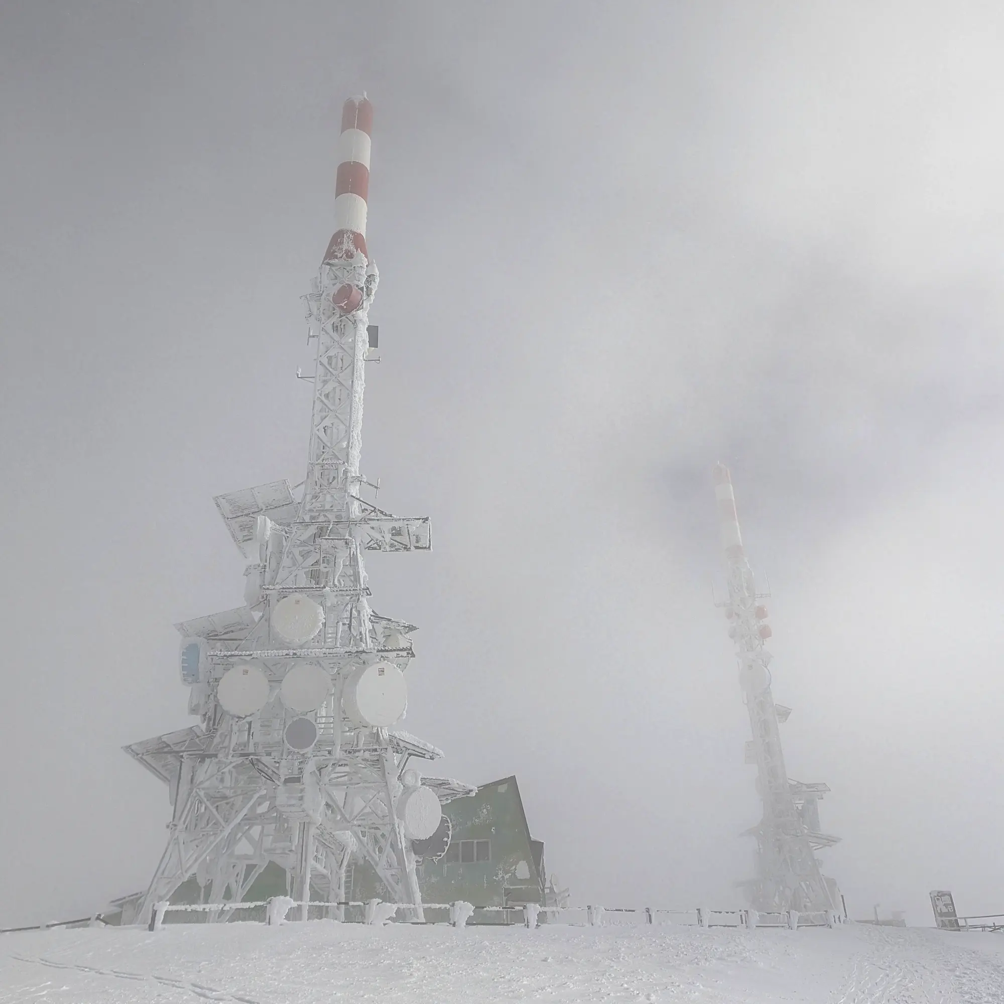 El cim de la Torreta de l'Orri, sota una espessa capa de neu i boira. Les torres de comunicació són a penes visibles. Cim nevat i boirós de la Torreta de l'Orri amb torres de comunicació poc visibles.