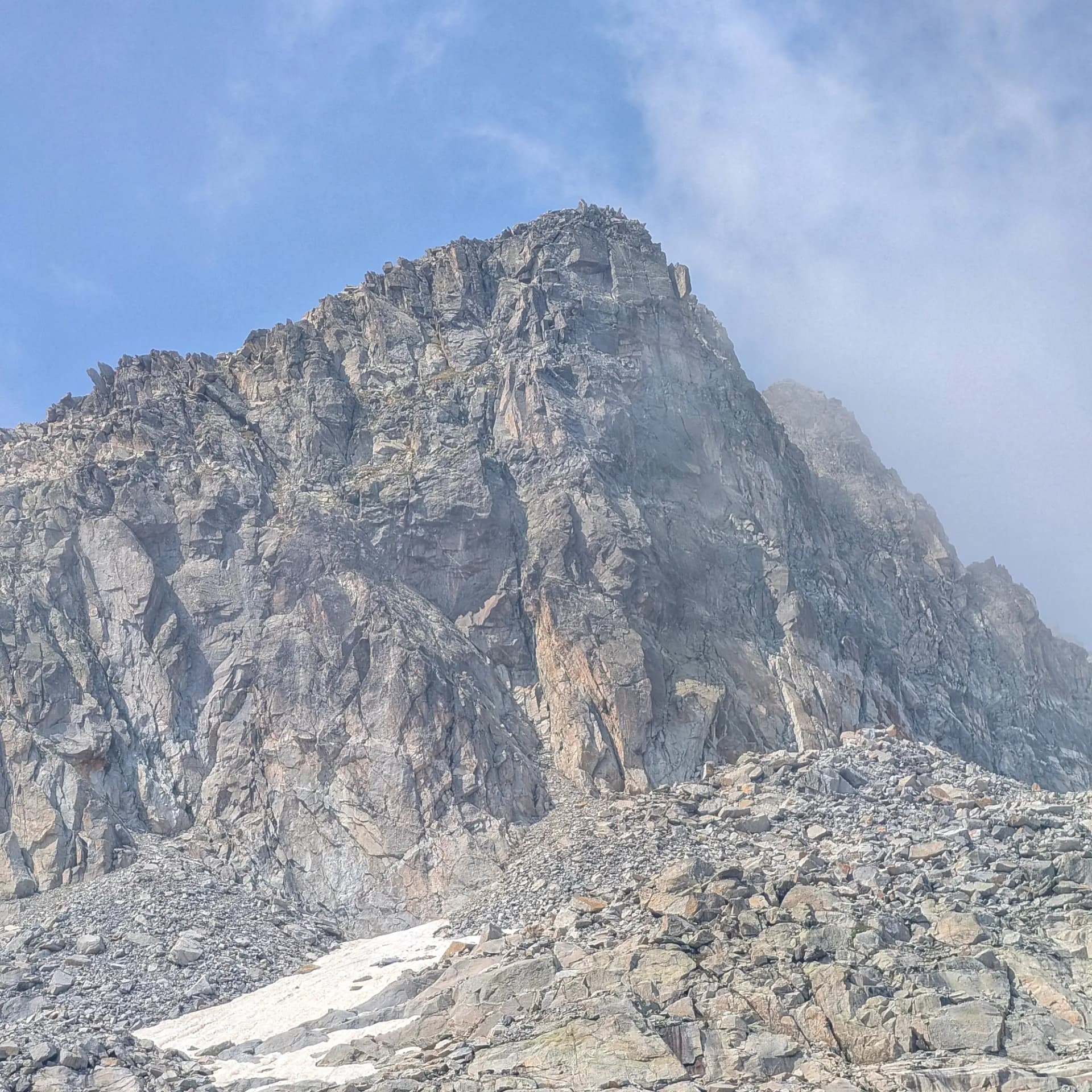 Rocoses pendents de granit i tarteres a la ruta d'ascensió al Pic de Comaloforno i Besiberri Sud als Pirineus. Una exigent travessa amb imponents formacions rocoses. Pic muntanyenc rocós de granit sota cel blau amb núvols lleugers. Tartera i clapes de neu a la base.