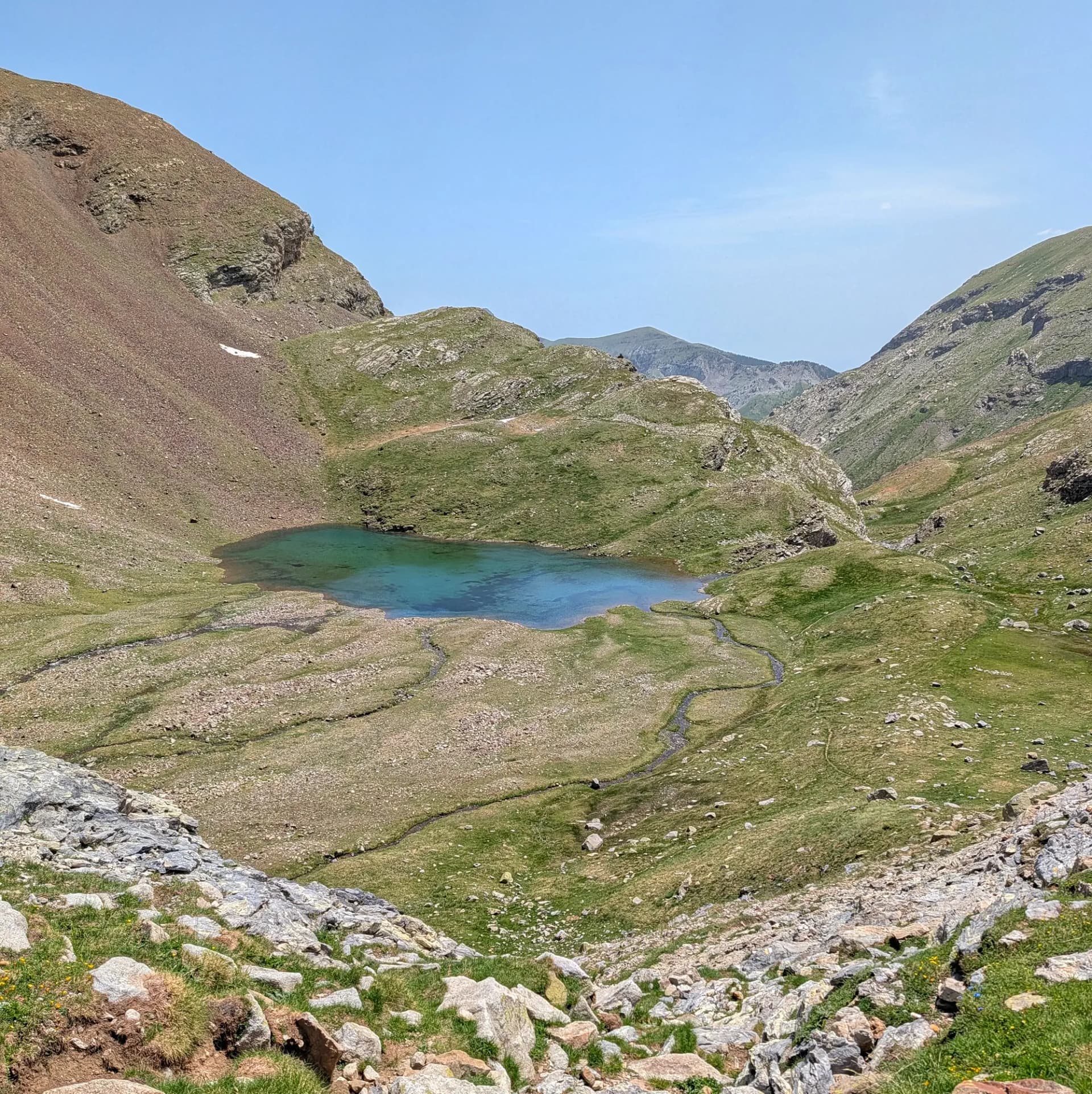 Les impressionants aigües turqueses de l'Ibon de Barbarisa, enlairat als Pirineus. Aquest bonic llac alpí forma part d'una desafiant ruta des del Collado de Sahún. Llac de muntanya turquesa envoltat de vessants verds i rocosos sota un cel blau clar, amb un petit rierol.