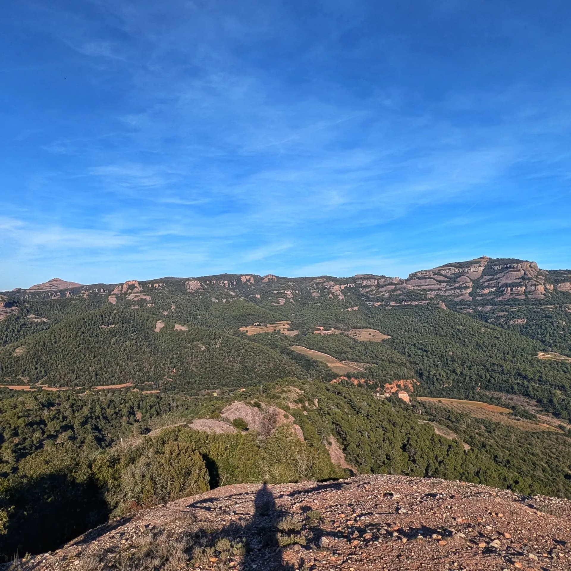 Vistas del Montcau y La Mola durante el ascenso a La Mola, en una ruta por el Parque Natural de Sant Llorenç del Munt i l'Obac. La ruta incluye el ascenso a La Mola, Montcau, Turó de la Pola y Castellsapera. Panorámica de las montañas Montcau y La Mola en el Parque Natural de Sant Llorenç del Munt i l'Obac bajo cielo azul.