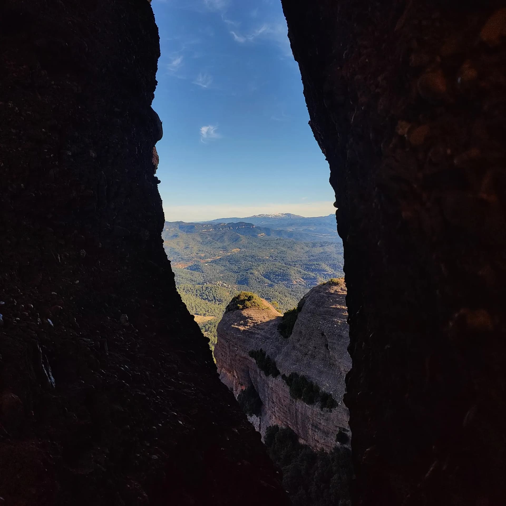 Vista panoràmica des del Morral del Drac, a Sant Llorenç del Munt, mostrant un paisatge muntanyós amb boscos frondosos i cims nevats al fons, emmarcada per roques. Vista des del Morral del Drac de Sant Llorenç del Munt, amb paisatge muntanyós, boscos verds i cims nevats, emmarcada per roques fosques.