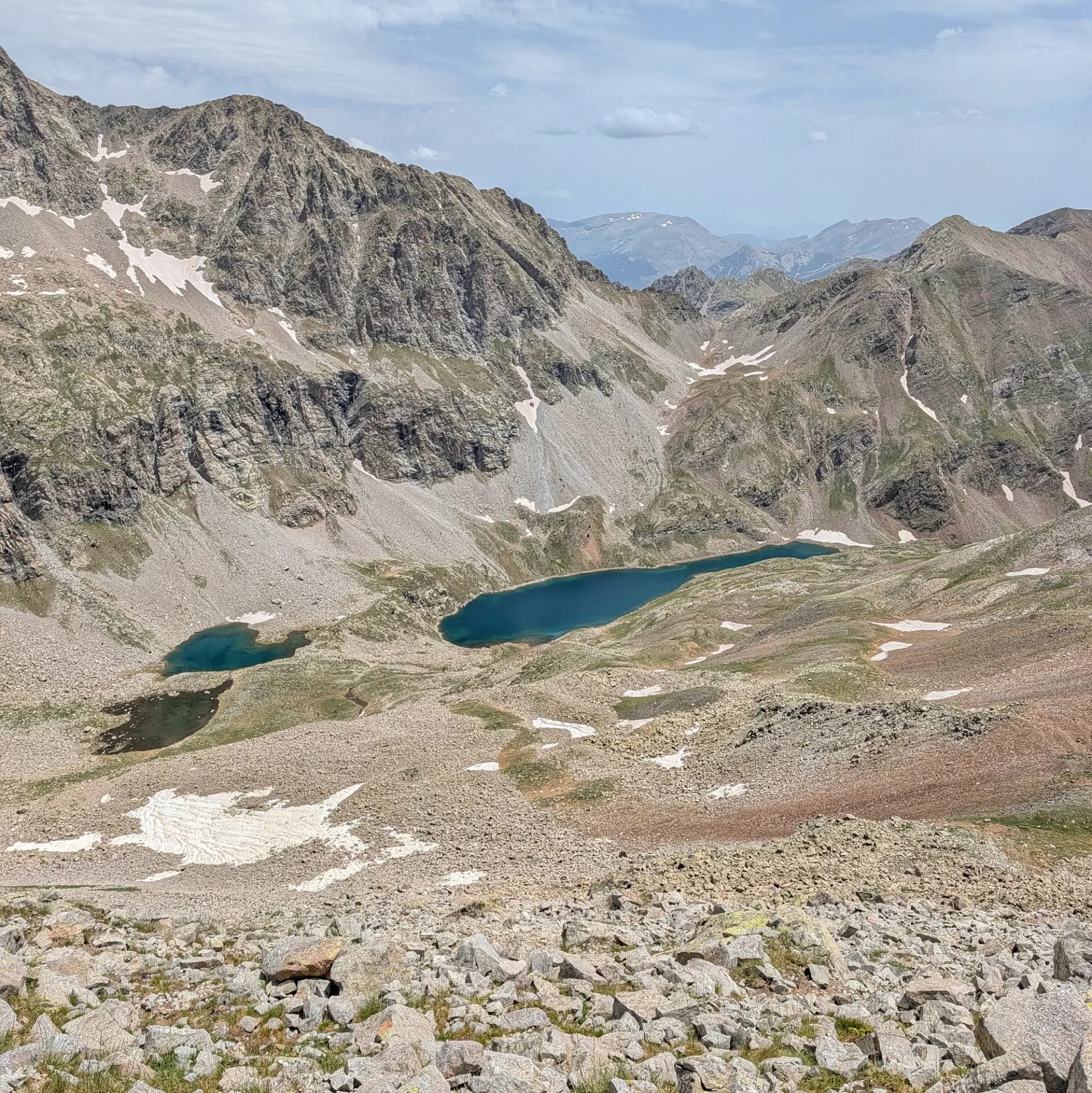 Impressionant vista dels Ibones de Barbarisa, als Pirineus. Aquest paisatge forma part de la ruta des del Collado de Sahún, mostrant llacs alpins i cims rocosos. Vista panoràmica de dos ibons alpins turquesa en una vall rocosa amb taques de neu sota un cel ennuvolat.