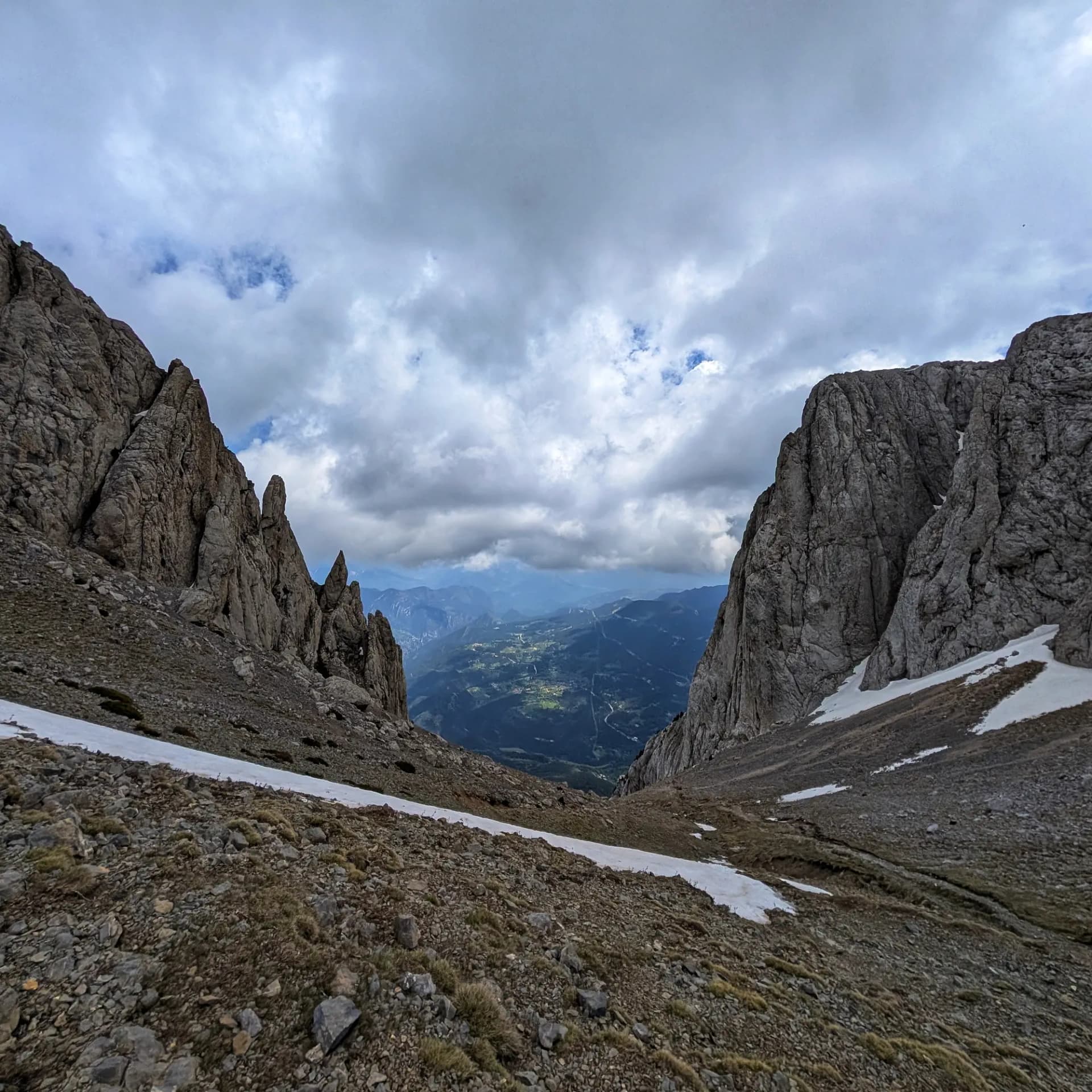 La Enforcadura del Pedraforca, un pas de muntanya distintiu que ofereix vistes panoràmiques a la vall sota un cel dramàticament ennuvolat, amb pendents rocosos i taques de neu. Pas de muntanya rocós de la Pedraforca amb neu i vistes a la vall sota un cel ennuvolat.