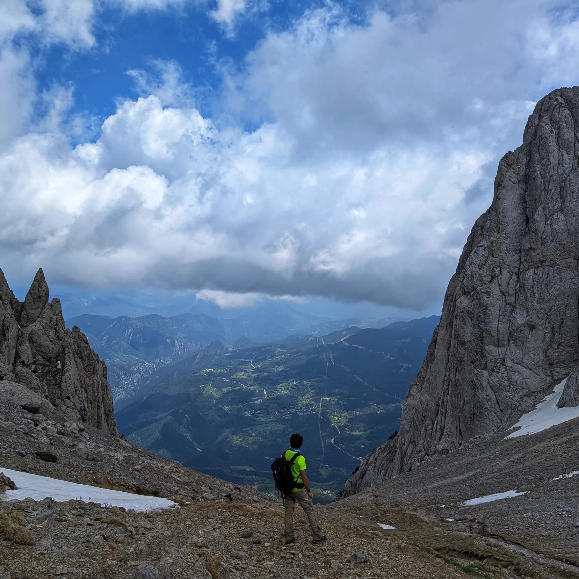 Enforcadura del Pedraforca, el coll entre els dos cims icònics del massís, contempla les valls extenses del Prepirineu català. Senderista amb samarreta lluminosa al coll rocós del Pedraforca, contemplant la vall i els cims sota un cel ennuvolat.