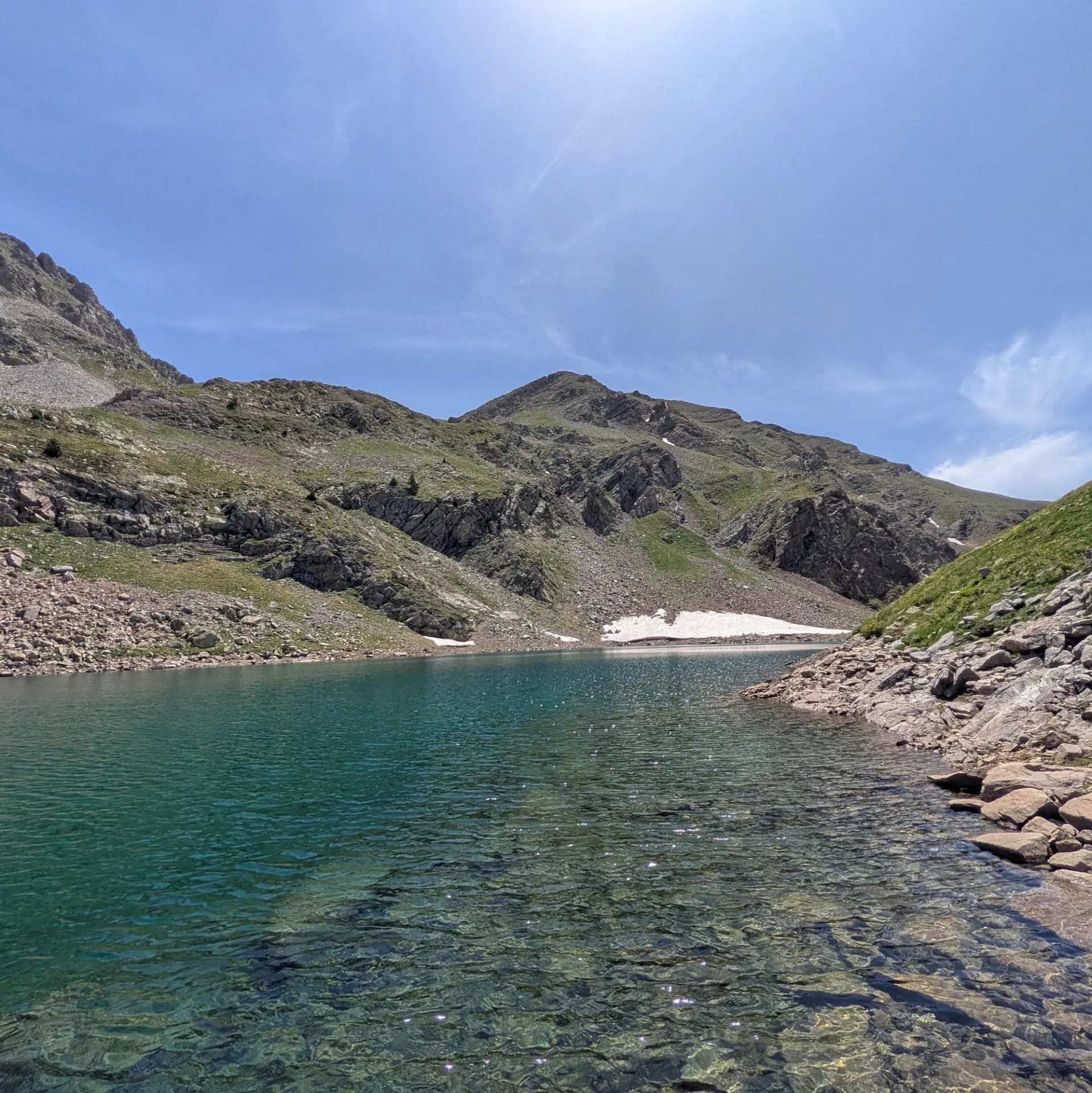 Les impressionants aigües turqueses de l'Ibon de Barbarisa, enclavat entre cims rocosos i vessants verds, amb congestes sota un cel blau vibrant. Una joia a la ruta des de Collado de Sahún. Llac de muntanya clar amb aigua turquesa, vora rocosa, vessants verds i congestes sota cel blau.