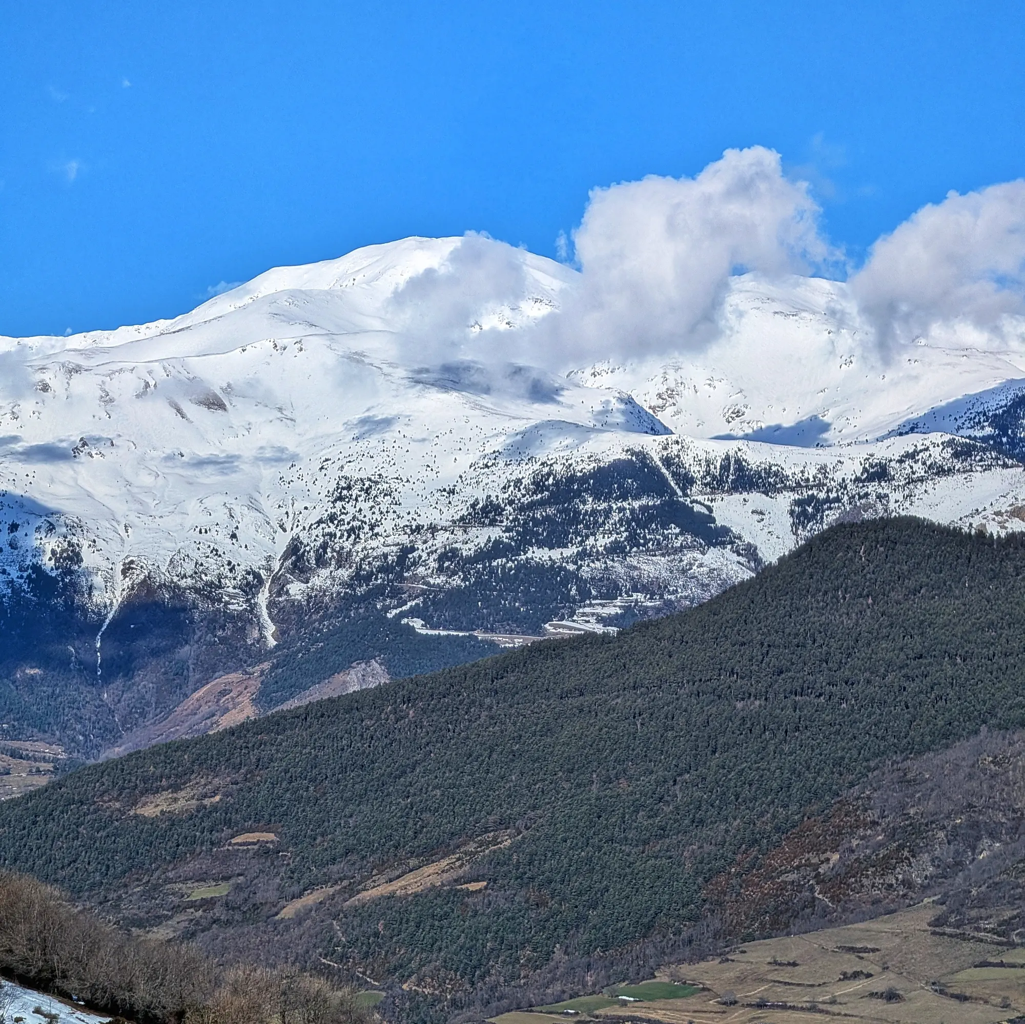 El Puigmal, completament nevat, es mostra amb els primers núvols baixos. La imatge va ser capturada durant l'ascens cap al Taga. Puigmal nevat amb núvols baixos, vist des de la pujada al Taga.